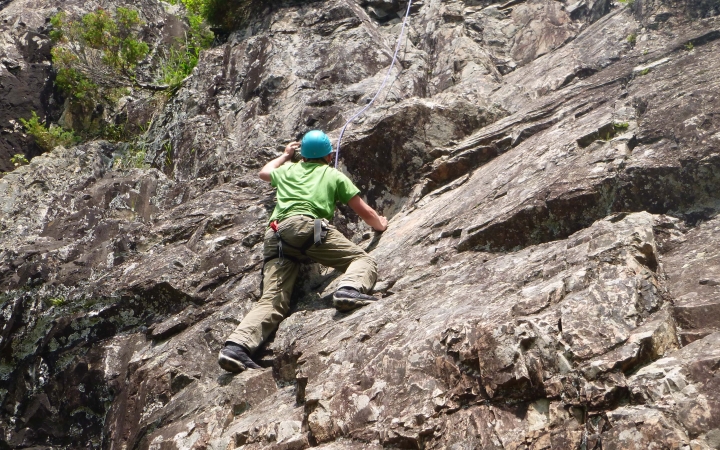 A person wearing safety gear and secured by ropes climbs up a rock wall.